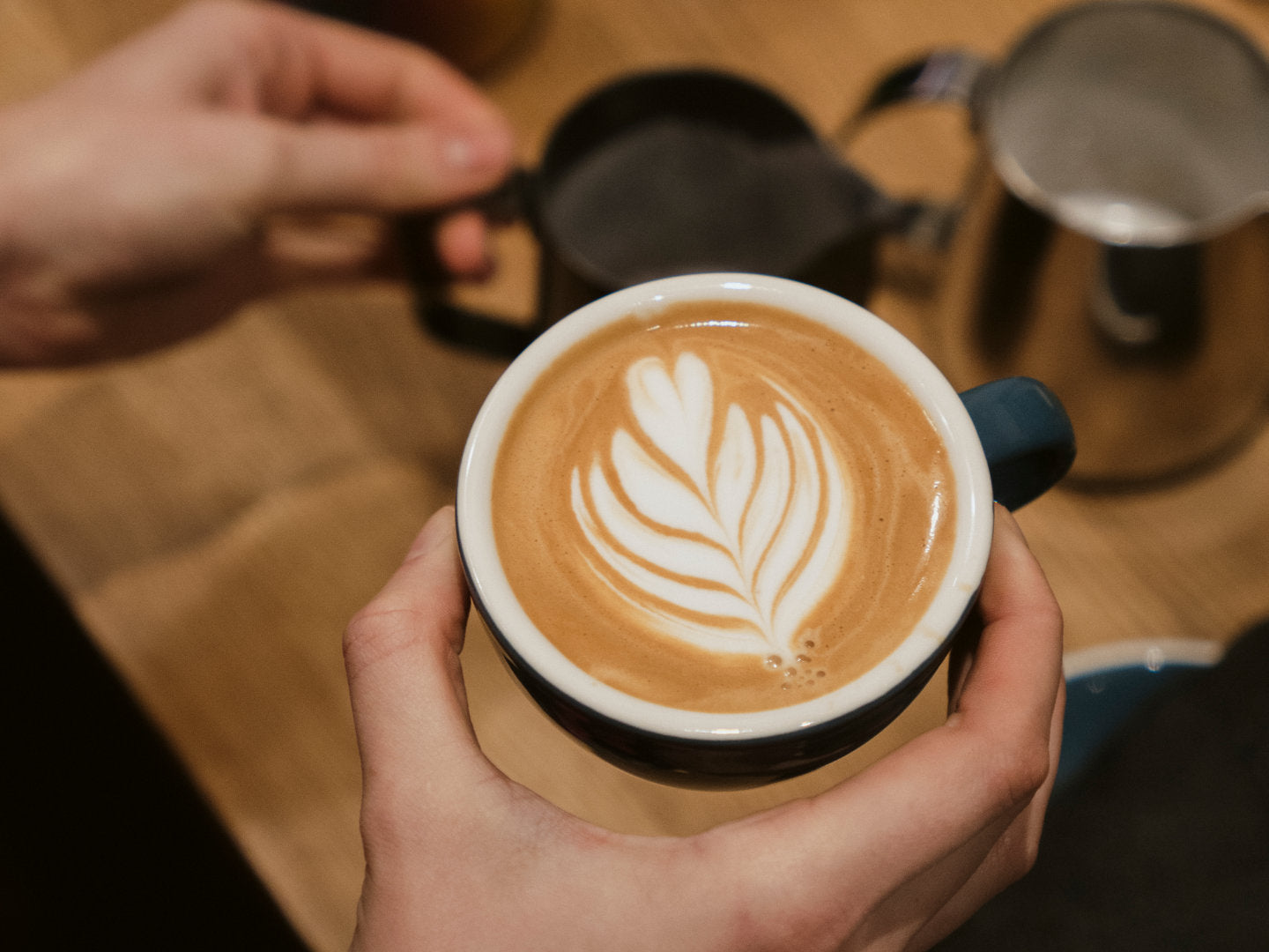 Titelbild zum Blogbeitrag "Anleitung für Cappuccino". Zu sehen ist ein Cappuccino in seiner Entstehung, bei der Milchschaum in den Kaffee geschüttet wird.