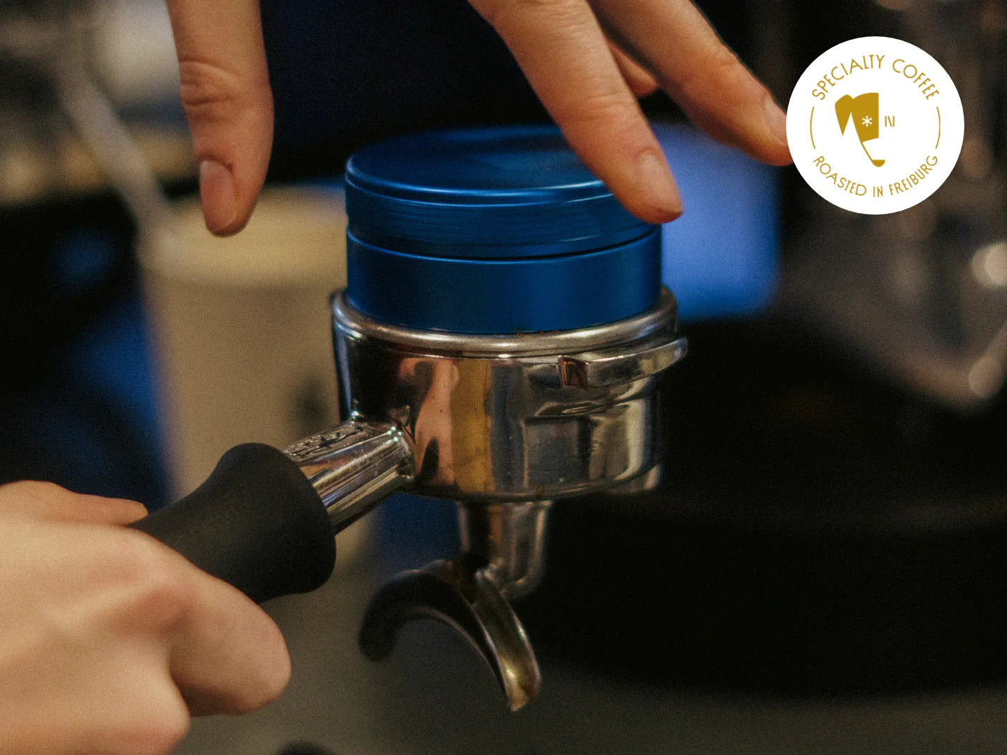 Titelbild des Artikels zur Espressozubereitung. Zu sehen ist ein Siebträger mit Kaffeemehl, der von zwei Händen gehalten wird. Auf dem Bild steht in weißer Schrift "Brew Guide".